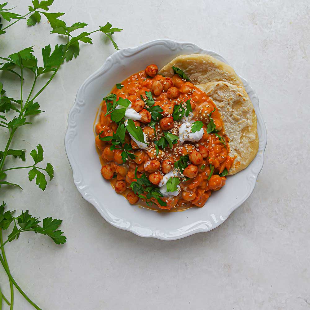 Kichererbsen-Tomaten-Curry mit Naan, frischen Kräutern, Kokosjoghurt und Sesam.