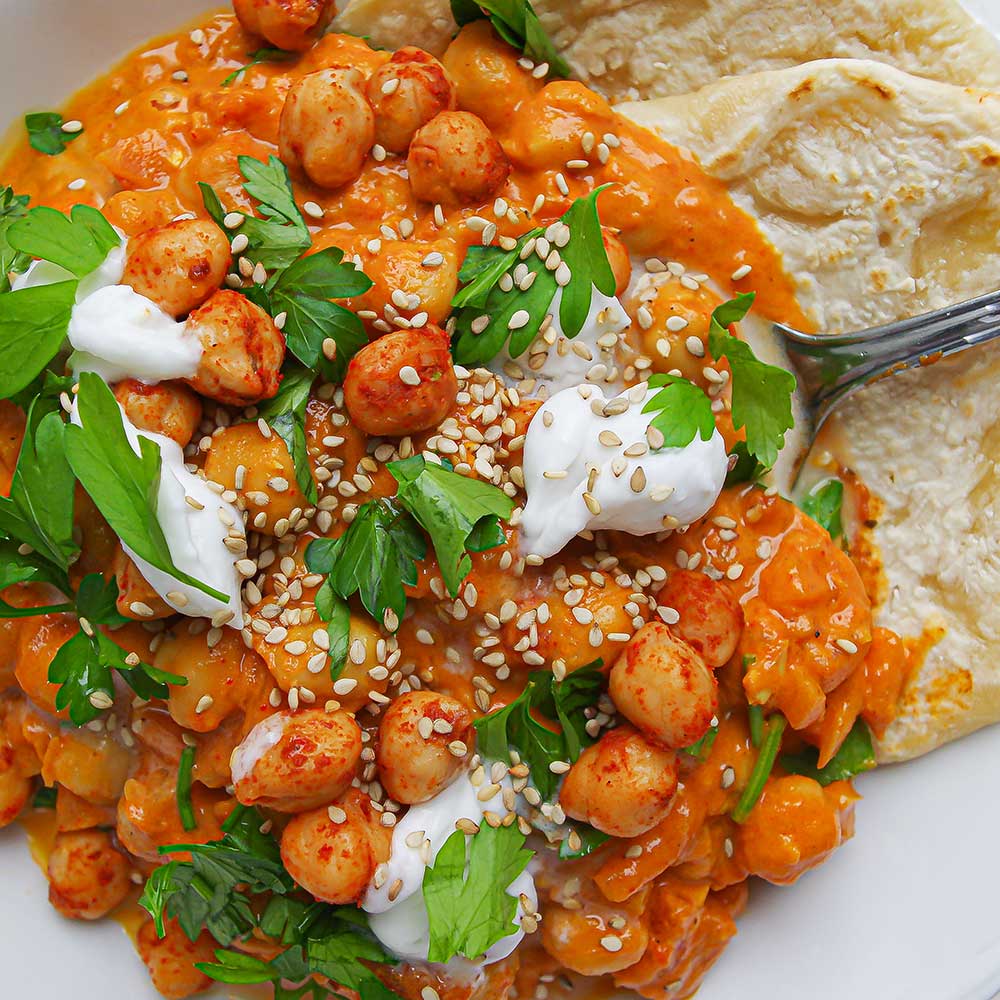 Kichererbsen-Tomaten-Curry mit Naan, frischen Kräutern, Kokosjoghurt und Sesam.