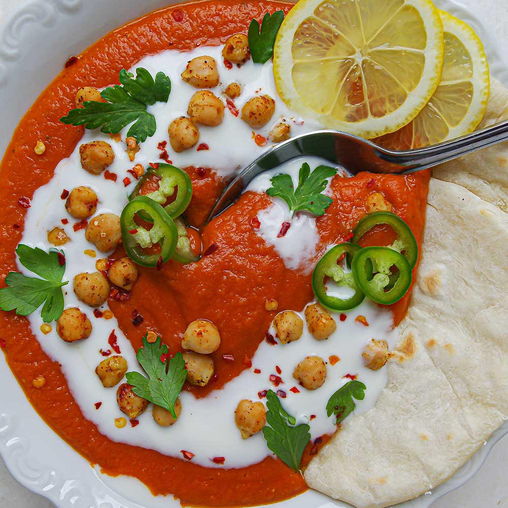 Kokos-Tomatensuppe mit roten Linsen mit Fladenbrot, Zitronenscheiben, frischen Kräutern, gerösteten Kichererbsen und Kokosjoghurt.