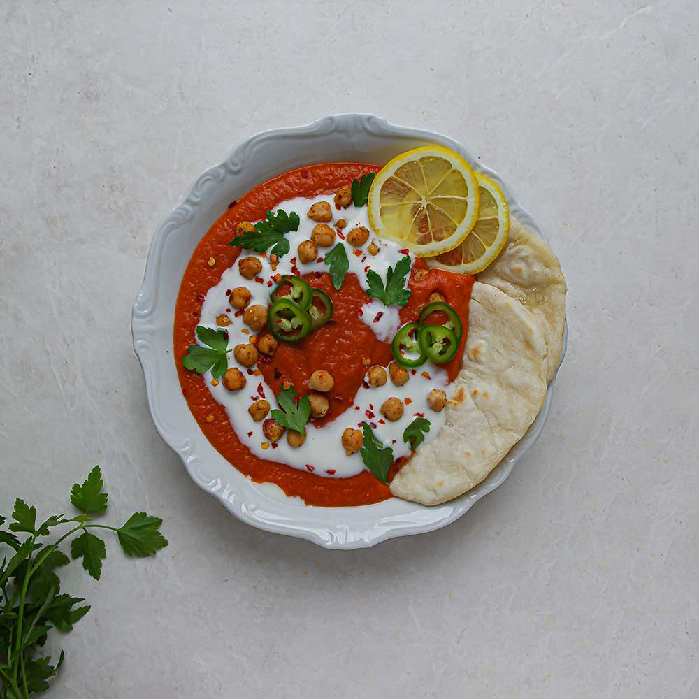 Kokos-Tomatensuppe mit roten Linsen mit Fladenbrot, Zitronenscheiben, frischen Kräutern, gerösteten Kichererbsen und Kokosjoghurt.