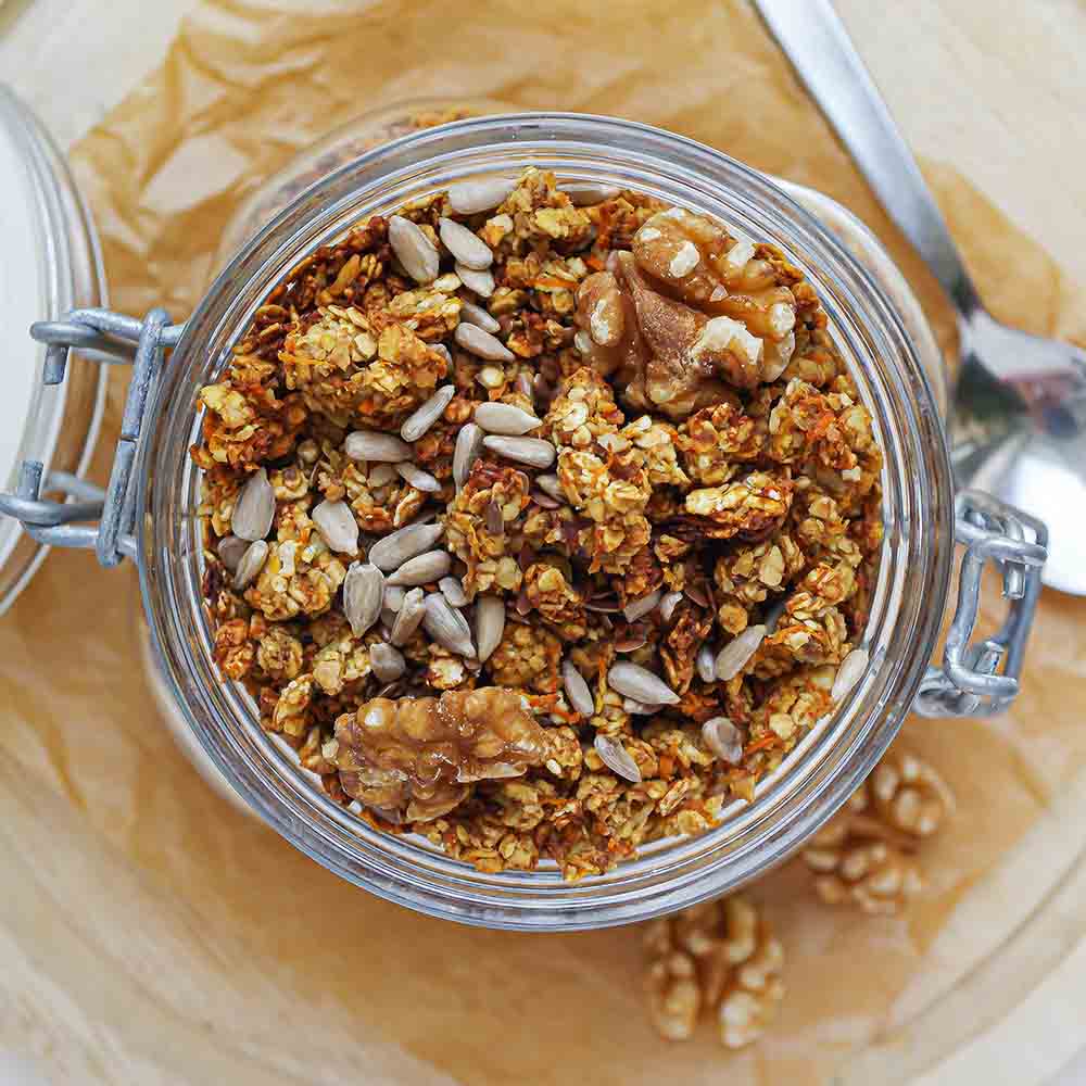 Knuspriges Karottenkuchen-Granola in einem Weckglas getoppt mit Sonnenblumenkernen und Walnüssen.