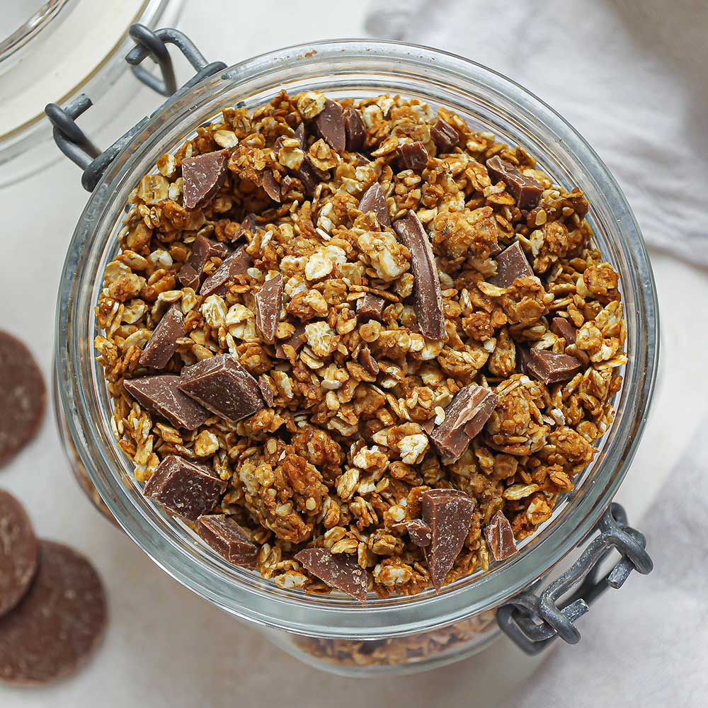 Eine Nahaufnahme von einem Schoko-Nuss-Granola getoppt mit gehackter Schokolade in einem Weckglas auf hellem Hintergrund.