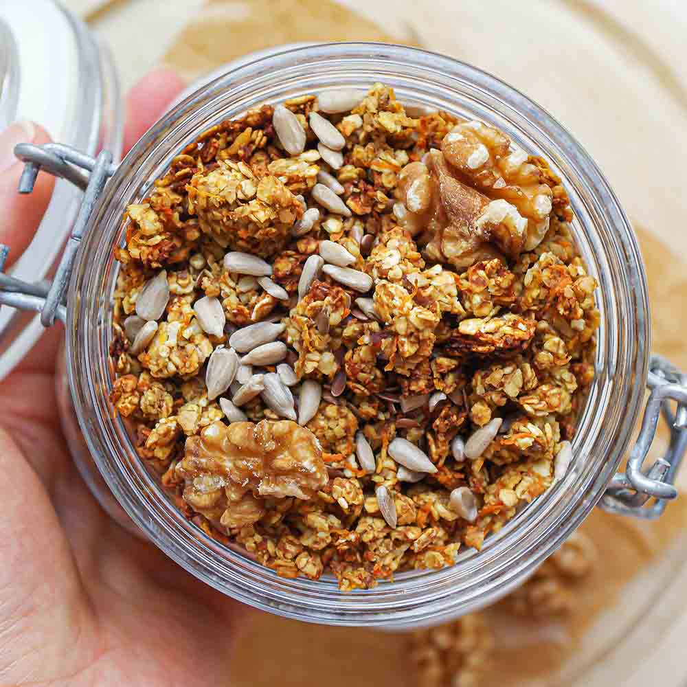 Knuspriges Karottenkuchen-Granola in einem Weckglas getoppt mit Sonnenblumenkernen und Walnüssen.