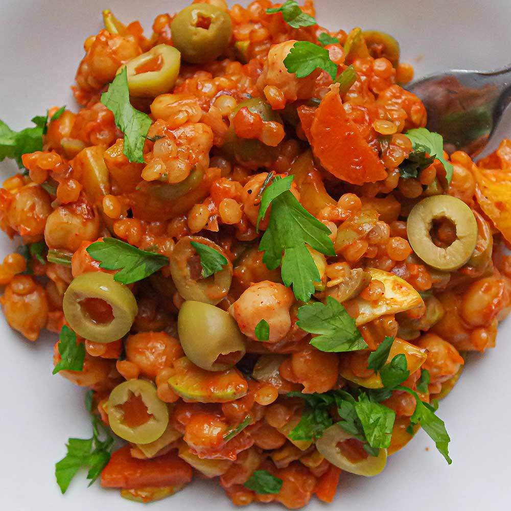 Eine Nahaufnahme von einer Mediterranen Couscous-Gemüsepfanne mit Oliven und frisch gehackter Petersilie.