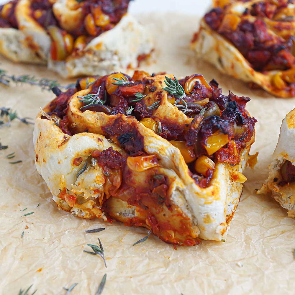 Pizza-Schnecken mit Tomaten-Mais-Füllung mit Thymian auf einem zerknitterten Backpapier. Die Pizza-Schnecken sehen sehr saftig, lecker und goldbraun gebacken aus. In der Füllung sie man den Mais, etwas Gemüse und das Tomatenmark.