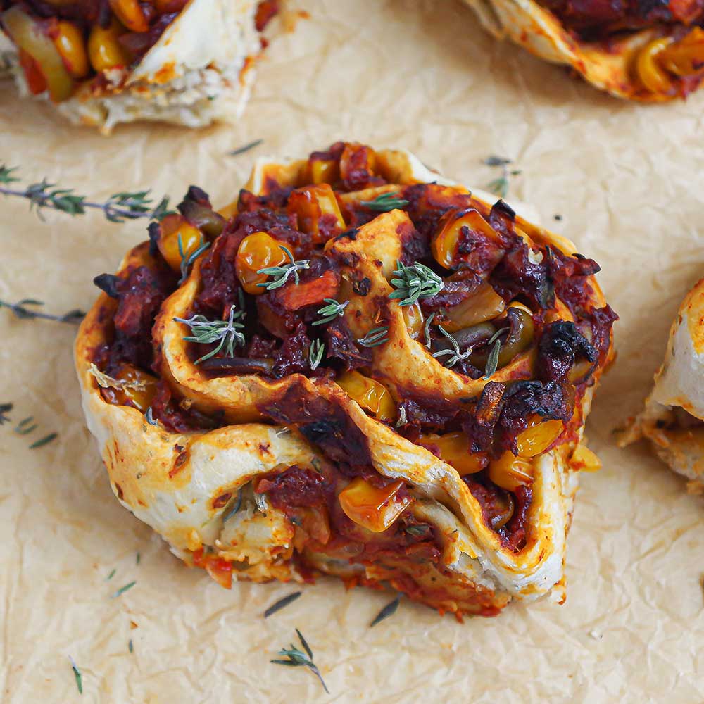 Pizza-Schnecken mit Tomaten-Mais-Füllung mit Thymian auf einem zerknitterten Backpapier. Die Pizza-Schnecken sehen sehr saftig, lecker und goldbraun gebacken aus. In der Füllung sie man den Mais, etwas Gemüse und das Tomatenmark.