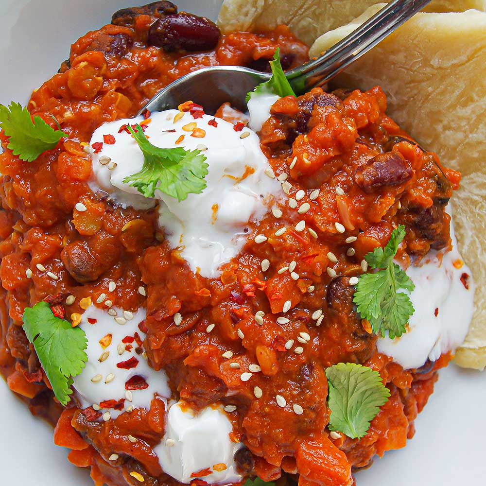 Eine Nahaufnahme von Proteinreichem Bohnen-Curry getoppt mit etwas Kokosjoghurt, Koriander und serviert mit Naan. 