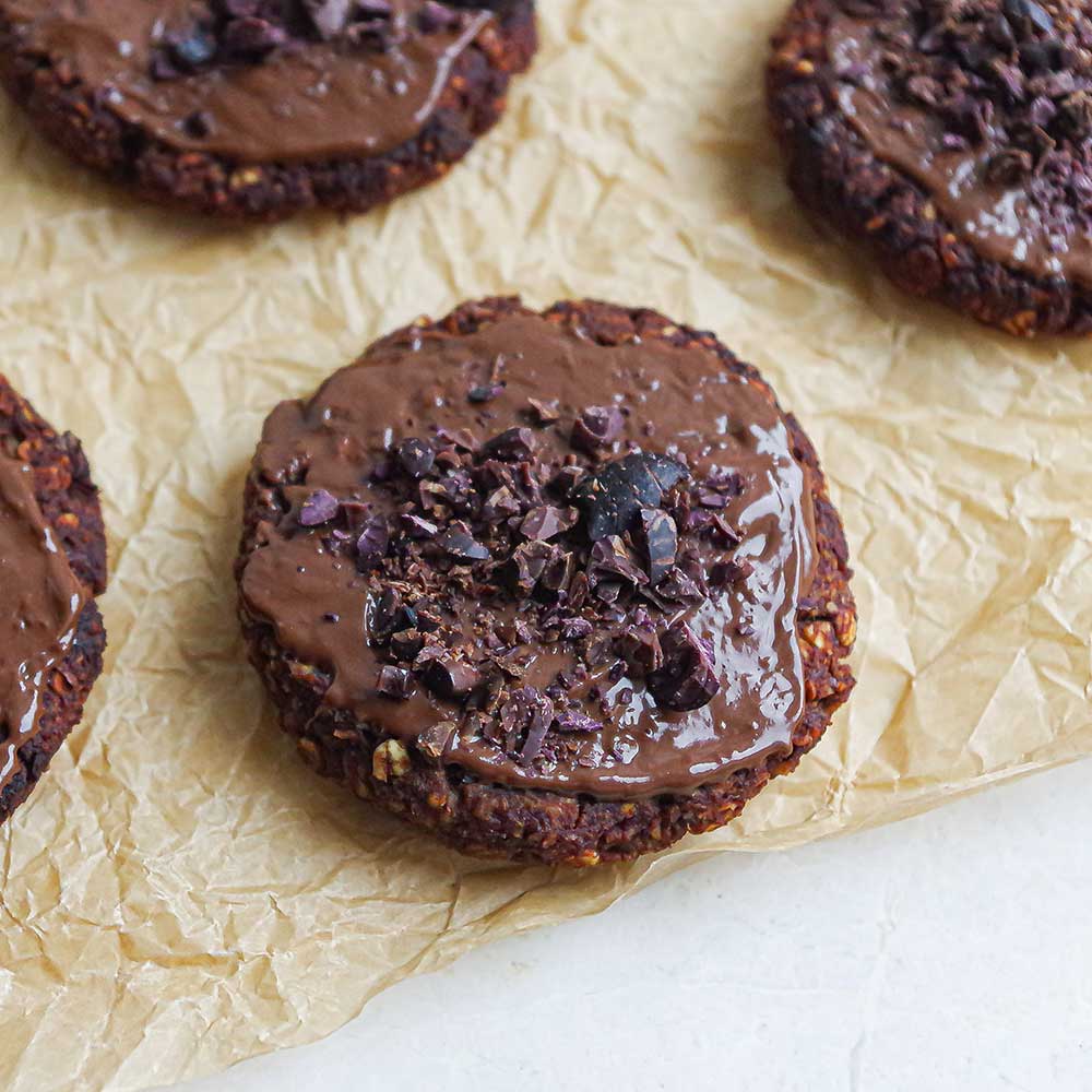 Weiche Schoko-Nuss-Cookies auf Backpapier mit Schokolade glasiert und Kakaonibs getoppt.