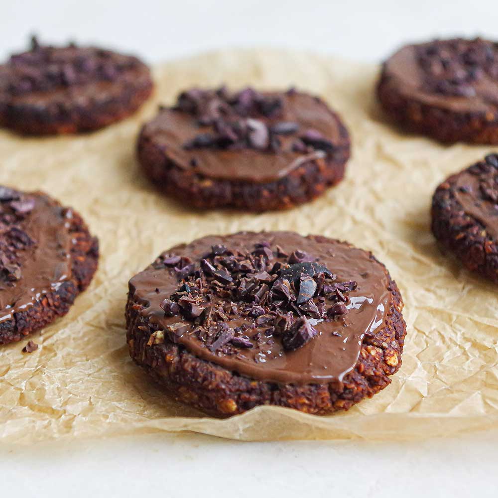 Weiche Schoko-Nuss-Cookies auf Backpapier mit Schokolade glasiert und Kakaonibs getoppt.