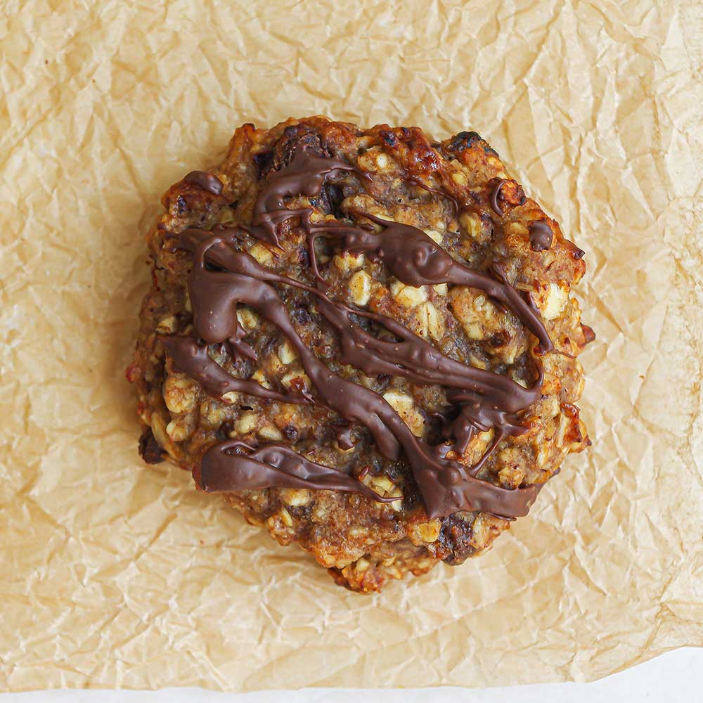 Eine Nahaufnahme eines braunen saftigen Bananenbrot-Cookies mit geschmolzener Schokolade verziert. Der Cookie liegt auf zerknittertem Backpapier.