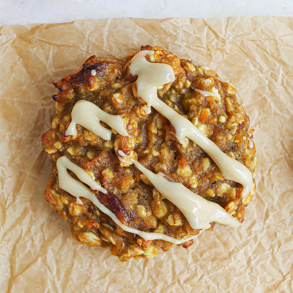 Eine Nahaufnahme aus der Vogelperspektive eines saftigen Karotten-Hafer-Cookies mit Rosinen und Cashewmus-Drizzle. Der Cookie liegt auf zerknittertem Backpapier.