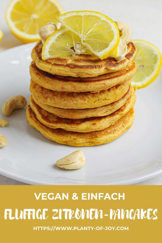 Fluffige Zitronen-Pancakes getoppt mit Zitronenscheiben und Cashews auf einem weißen Keramikteller. Im Hintergrund sind halbe Zitronen. Die Pancakes sehen sehr saftig und lecker aus und haben eine gold-gelbe Farbe. Der untere Teil des Bildes ist gelb mit weißem Text. Der Text lautet vegan & einfach, Fluffige Zitronen-Pancakes und die url der Website Planty of Joy.