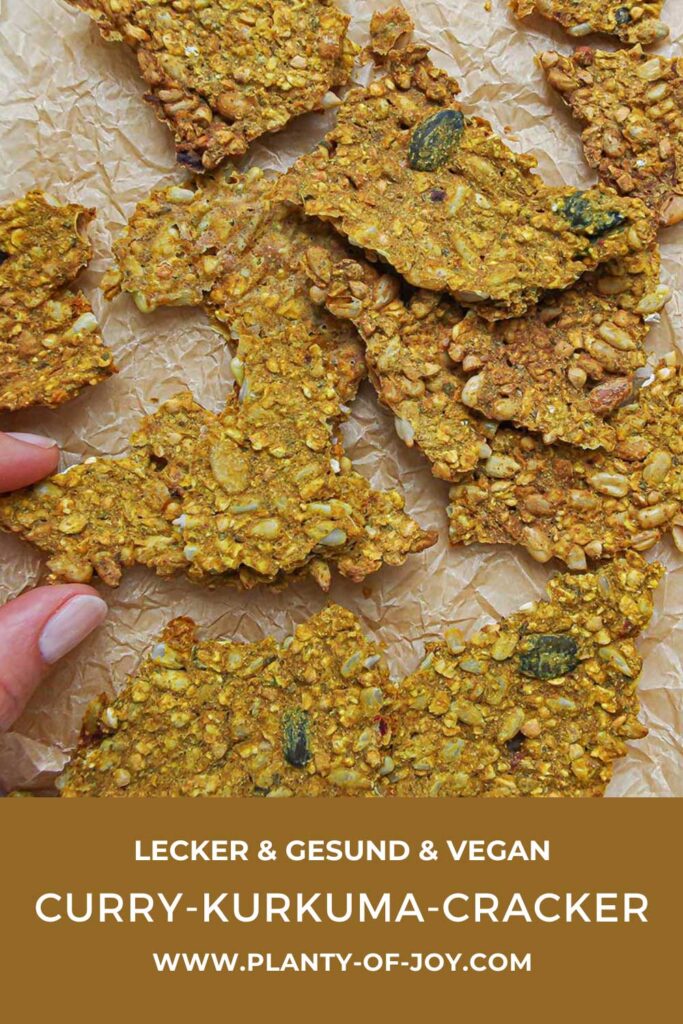 Curry-Kurkuma-Cracker auf Backpapier. Die Cracker sehen sehr knusprig und lecker aus mit vielen Saaten, Kernen und Samen. Der untere Teil des Bildes ist braun mit weißem Text. Der Text lautet lecker,& gesund & vegan, Curry-Kurkuma-Cracker und die url der Website Planty of Joy.