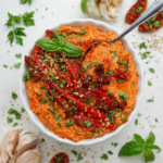 Cremiger Paprika-Tofu-Aufstrich in einer Schüssel mit gerösteter Paprika, getrockneten Tomaten, Sesam und frischen Kräutern