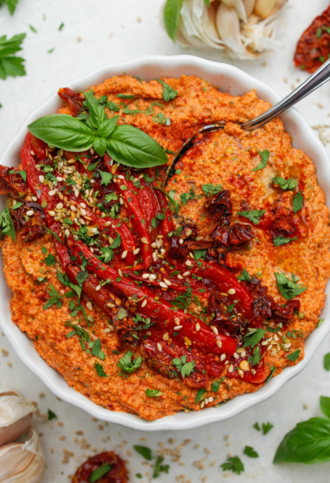 Cremiger Paprika-Tofu-Aufstrich in einer Schüssel mit gerösteter Paprika, getrockneten Tomaten, Sesam und frischen Kräutern